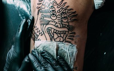 partial view of tattoo artist in gloves working on tattoo on shoulder in salon